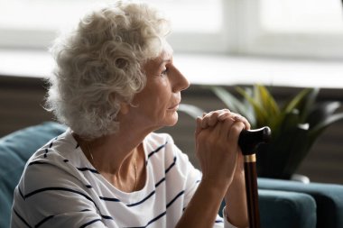 Tahta baston tutan, sorunlarını düşünen düşünceli olgun kadın.