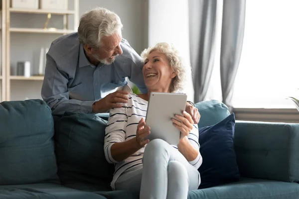 Excited older man and woman having fun with computer tablet