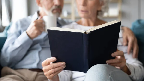 Close up older couple reading book together at home