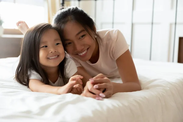 Felice madre asiatica sdraiata a letto insieme a piccola figlia — Foto Stock