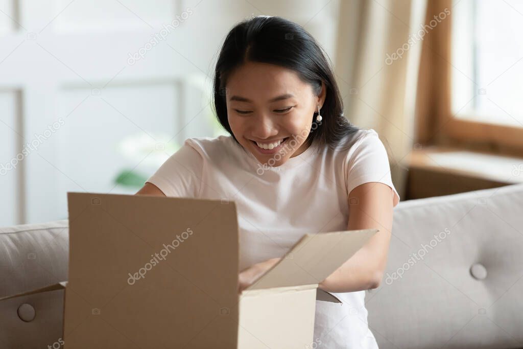 Vietnamese woman sitting on sofa opens delivered parcel feels happy