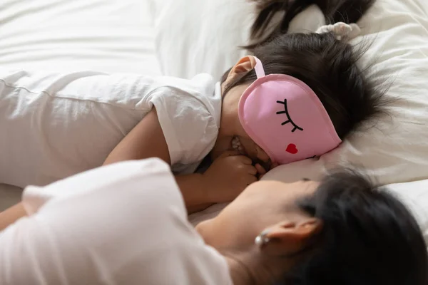 Niña pequeña usa máscara de dormir acostada en la cama con la madre — Foto de Stock