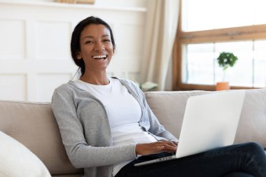 Kanepeye oturup dizüstü bilgisayar kullanan Afrikalı Amerikalı bir kız.