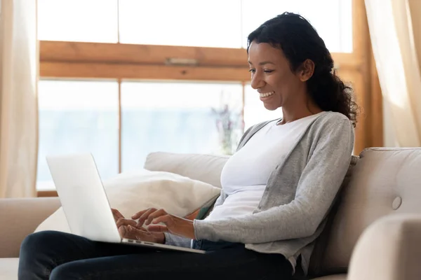 Uśmiechnięty czarny kobieta trzymać laptop na kolanach i pisania — Zdjęcie stockowe