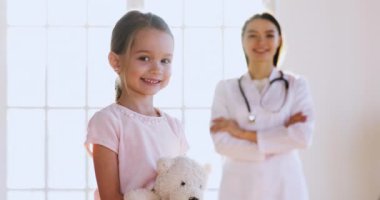 Arka planda kadın çocuk doktoruyla oyuncak tutan mutlu küçük kız..