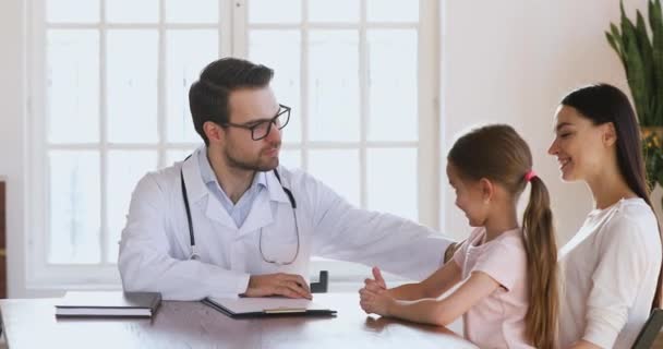 Amical jeune pédiatre masculin parlant à une petite fille patiente . — Video