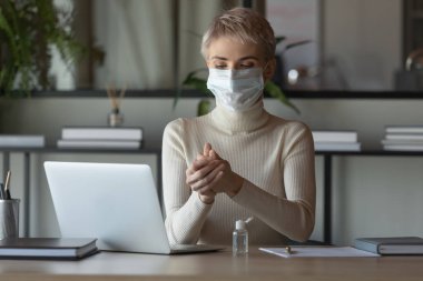 Kadın çalışan işyerinde dezenfektanla ellerini temizliyor