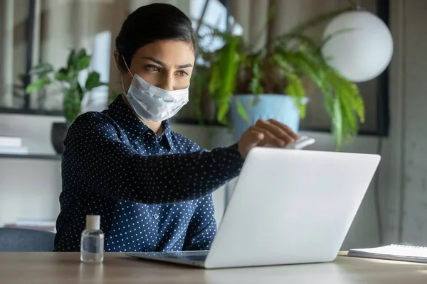 Female employee in face mask disinfect laptop with sanitizer — Stock Photo, Image