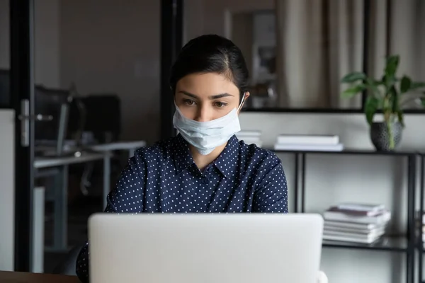 Empleada en el trabajo de máscara facial en el ordenador portátil en la oficina — Foto de Stock