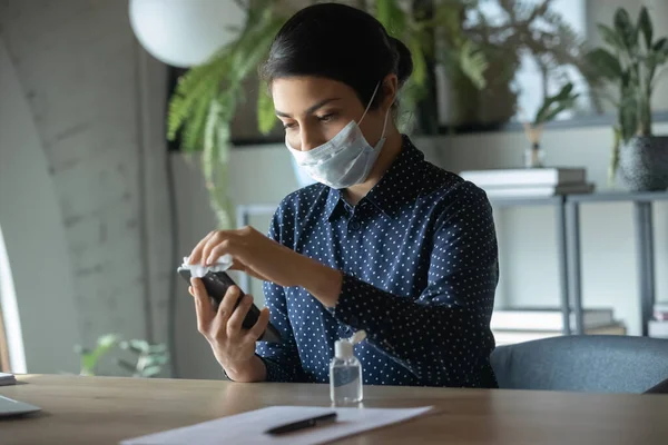 Mujer en mascarilla facial desinfectar celular con desinfectante — Foto de Stock