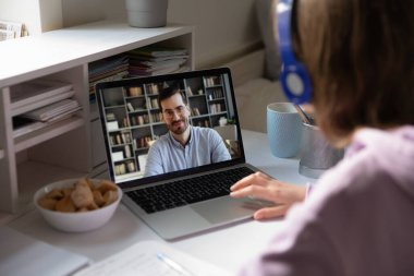 Kulaklık takan öğrenci kız, masada oturmuş eğitici web sitelerini izliyor.