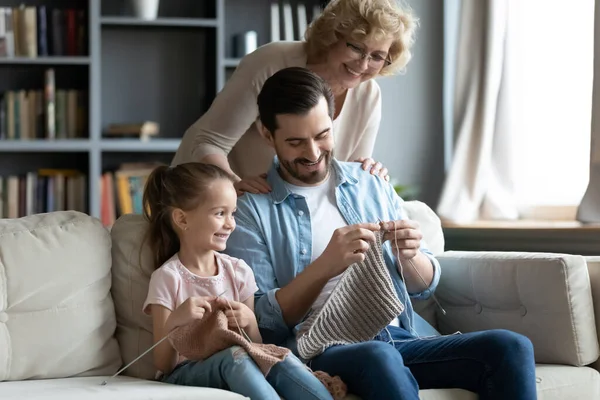 Multi-generational family enjoy common hobby knitting seated on couch