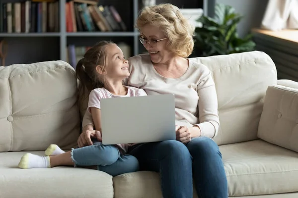 Grandmother and granddaughter having fun using laptop watching cartoons online