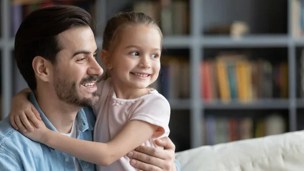 Little daughter seated on father lap hugs him looking aside — Stock Photo, Image