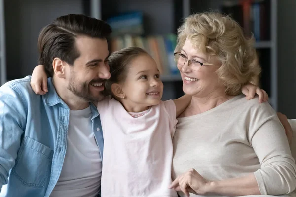 Liten flicka kramar far tittar med kärlek på äldre mormor — Stockfoto