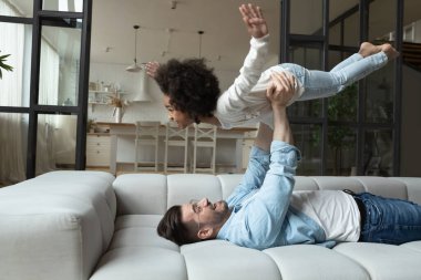 Önemseyen genç Kafkasyalı baba evde melez küçük kızıyla uçağın taklidini yaparken iyi eğlenceler.