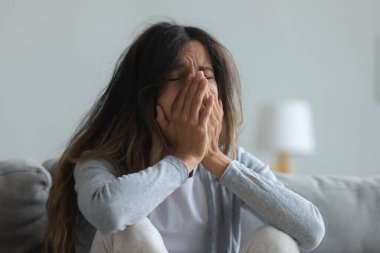 Depresyondaki genç kadın ağlıyor, elleri kapalı yüzünü kapatıyor.