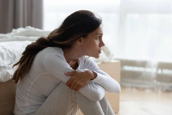 Droevige vrouw die knieën omarmt, op de vloer zit, zich depressief voelt — Stockfoto