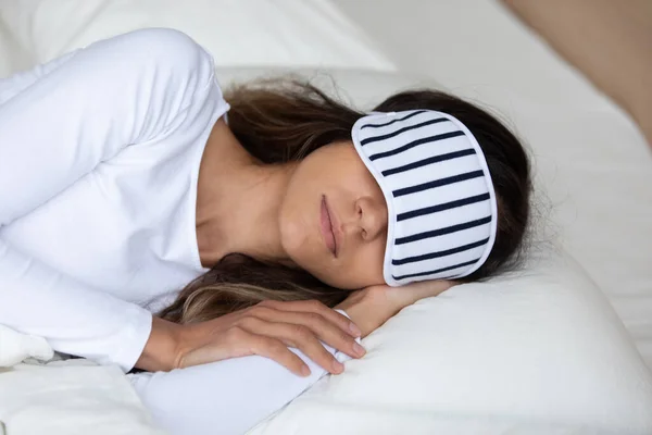 Woman wearing sleeping mask resting with hand under cheek