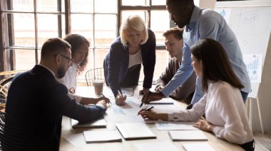 Çok ırklı meslektaşlar toplantıda evrak işlerini tartışırken beyin fırtınası yapıyorlar.
