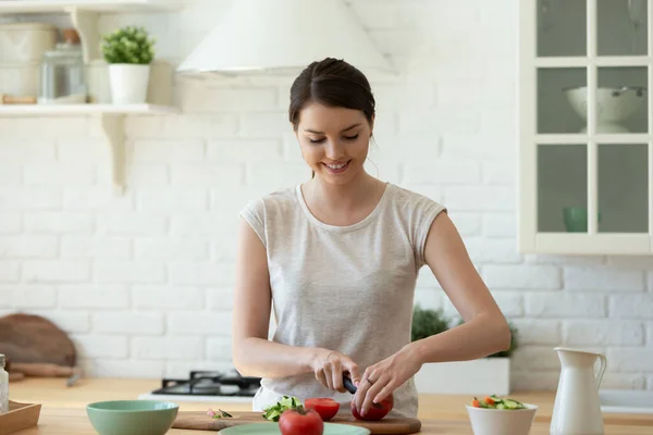 Happy attractive woman chopping vegetables for cooking salad.