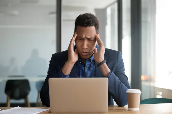 African businessman sitting at desk touch temples suffers from headache