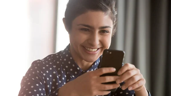 Happy indian woman holding smartphone looking at screen reading message