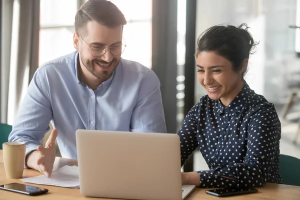 Multi-etnische collega 's zitten aan het bureau grapjes te maken op de werkplek — Stockfoto