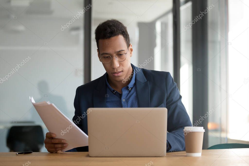African ethnicity businessman checking documents using laptop working in office