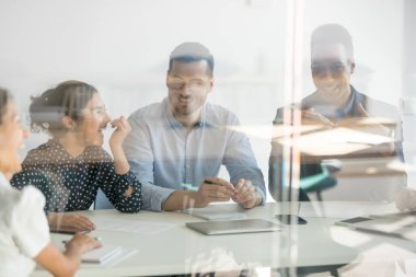 Farklı etnik köken çalışanları toplantı odasında sabah brifinginde gülüyorlar.