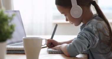 Kulaklık takan güzel bir ilkokul kızı evde öğreniyor.