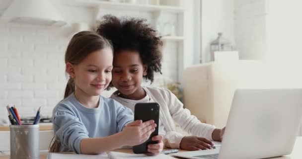 Два счастливых милых разнообразных этнических ребенка, использующих смартфон дома — стоковое видео