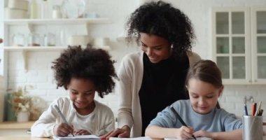 Afrikalı anne, bebek bakıcısı ev ödevlerini kontrol ediyor çeşitli etnik kökenli çocuklara yardım ediyor