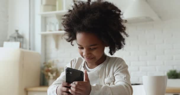 Linda niña africana sosteniendo teléfono inteligente disfrutando usando aplicaciones móviles — Vídeo de stock