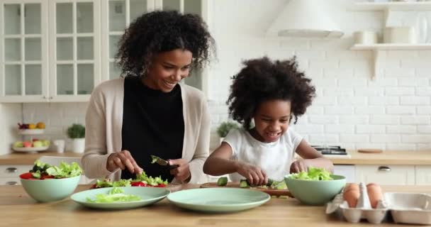 Adorable african daughter helping mum cutting vegetable salad in kitchen — Stock Video