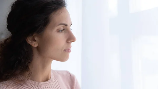 Thoughtful young woman looking away through window.