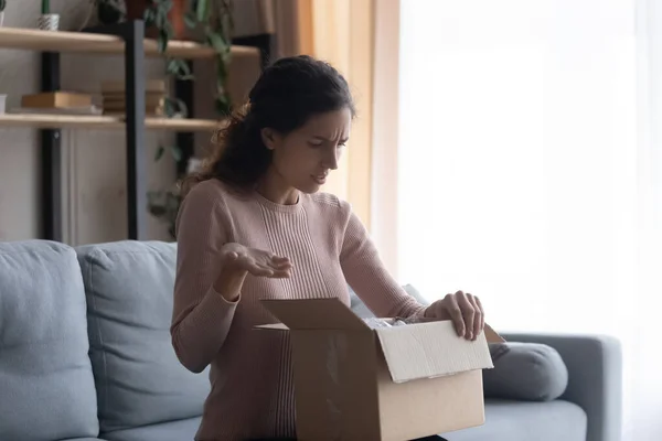 Stressed frowning young woman looking inside cardboard box, feeling dissatisfied.