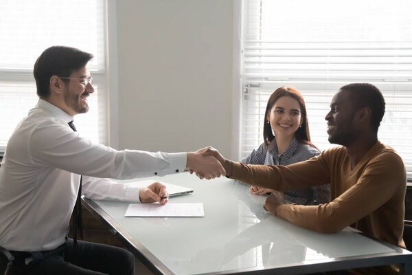 Smiling african american husband shaking hands with businessman for signing.