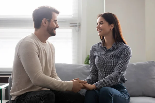 Happy young man holding attractive woman hands on couch. — Stock Photo, Image