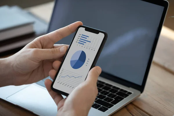 Close up businessman holding phone with diagrams on screen