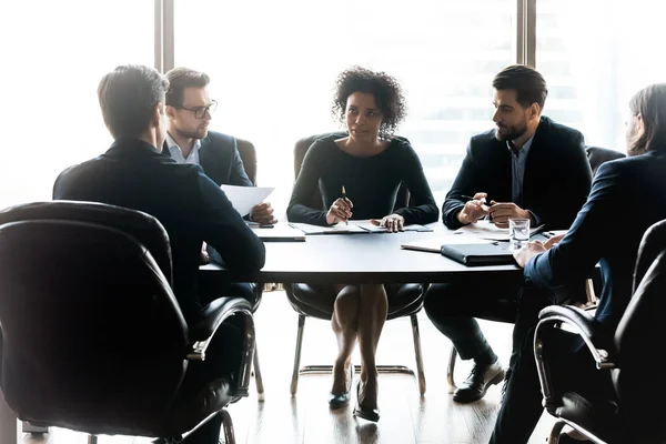 Diverse business partners discussing project, sitting at table in boardroom