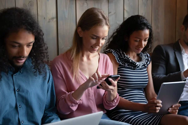 Multiracial young people relax on sofa using devices