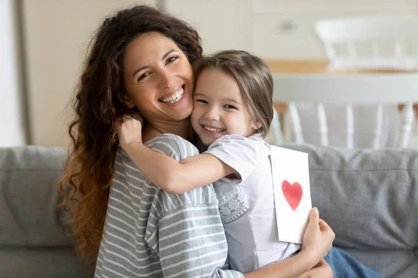 Lächelndes kleines Mädchen umarmt junge Frau und bereitet Grußkarte vor. — Stockfoto