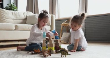 İki sevimli kız kardeş yerde oturmuş tahta bloklar oynuyorlar.