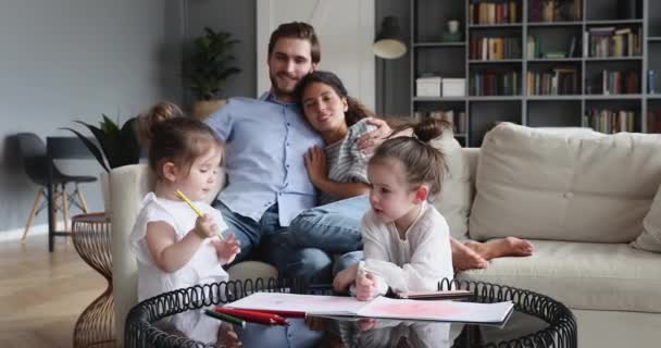 Zwei entzückende Töchter zeichnen, während glückliche Eltern auf dem Sofa lümmeln — Stockvideo