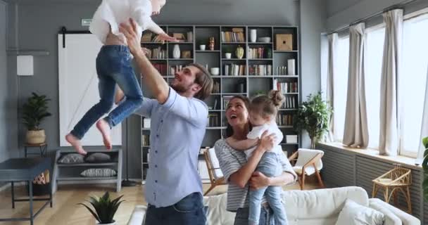Młodzi rodzice grający w aktywną grę z dziećmi rzucającymi córkami w górę — Wideo stockowe