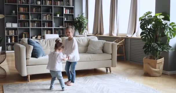 Zwei glückliche Kindermädchen, die Händchen halten und im Wohnzimmer tanzen — Stockvideo