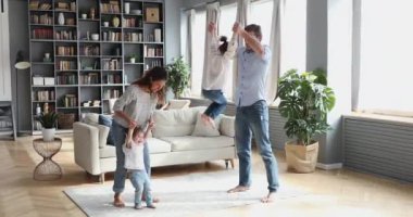 Modern oturma odasında çocuklarla dans eden mutlu ebeveynler.