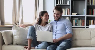 Genç mutlu çift kanepede oturup dizüstü bilgisayar kullanarak eğleniyor.