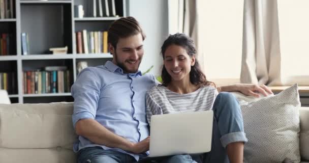 Uśmiechnięta, zrelaksowana młoda para korzystająca z laptopa w domu na kanapie — Wideo stockowe